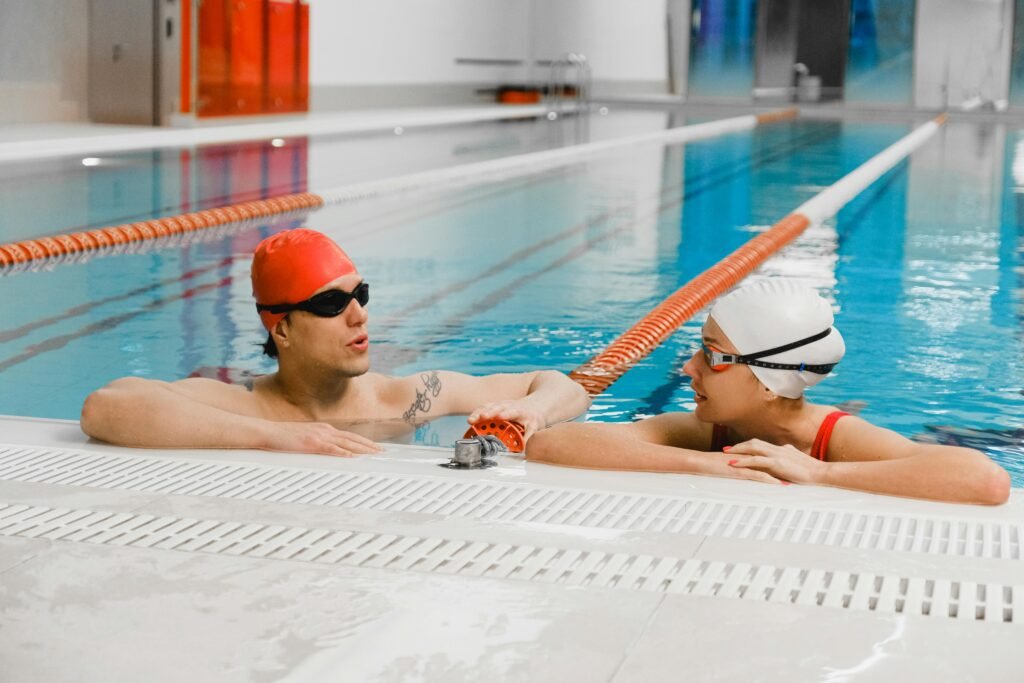 Swimmers with caps and goggles conversing at the edge of an indoor pool.